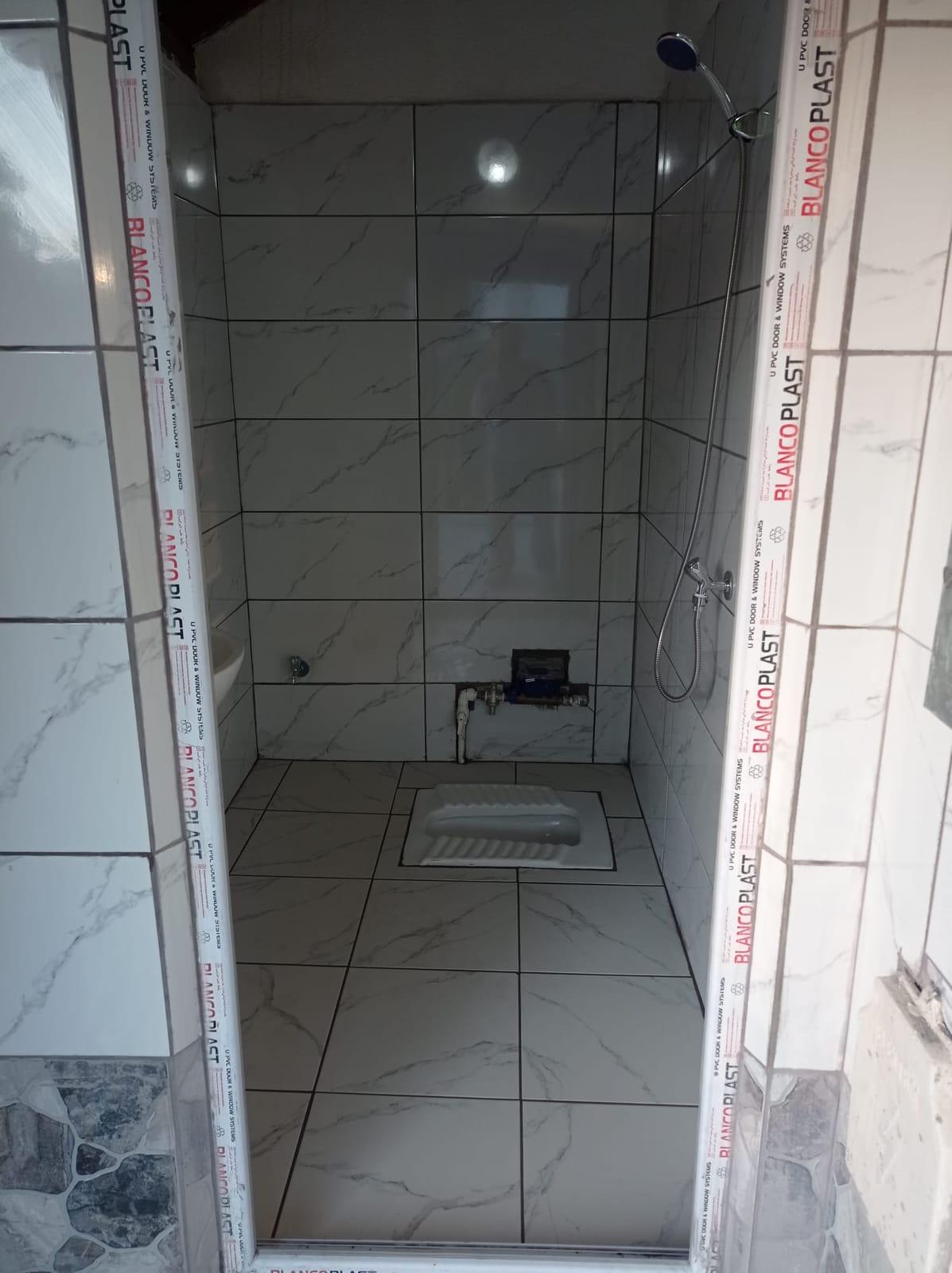 Duvarları ve zemini beyaz mermer desenli seramikle kaplanmış banyo